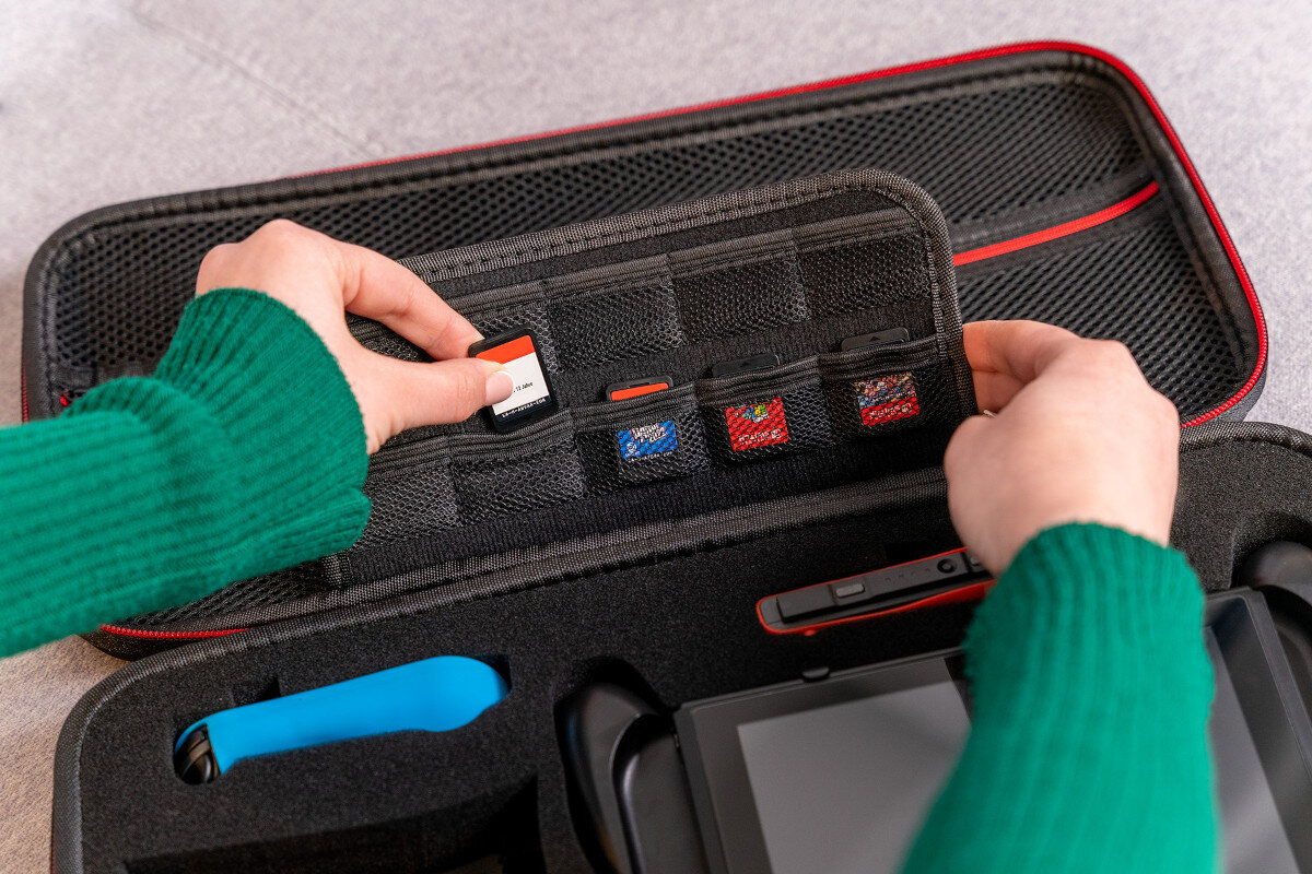 Osoba wkłada kartę pamięci do czarnego etui z kilkoma przegródkami na karty. W etui znajduje się również urządzenie elektroniczne z ekranem.