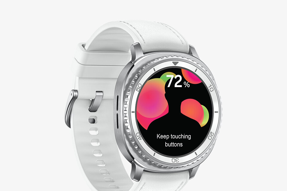 Smartwatch z białym paskiem i srebrną kopertą, na wyświetlaczu widoczny jest kolorowy motyw z tekstem \'72%\' oraz \'Keep touching buttons\'.