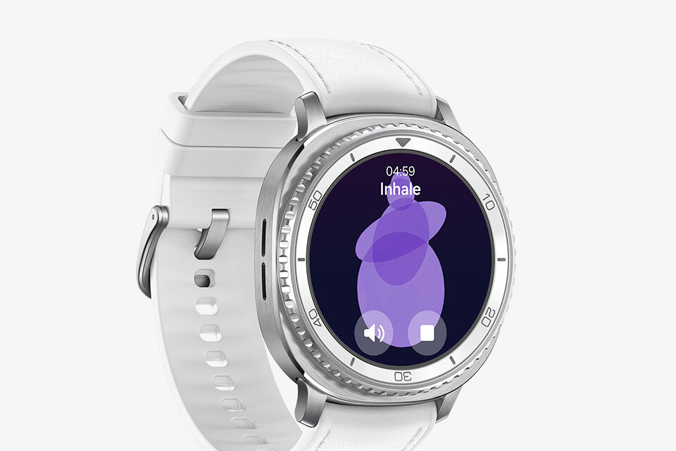 Smartwatch z okrągłą tarczą i białym paskiem, na ekranie widoczny jest napis \'Inhale\' oraz czas 04:59. Tarcza ma srebrną obwódkę z oznaczeniami minutowymi.