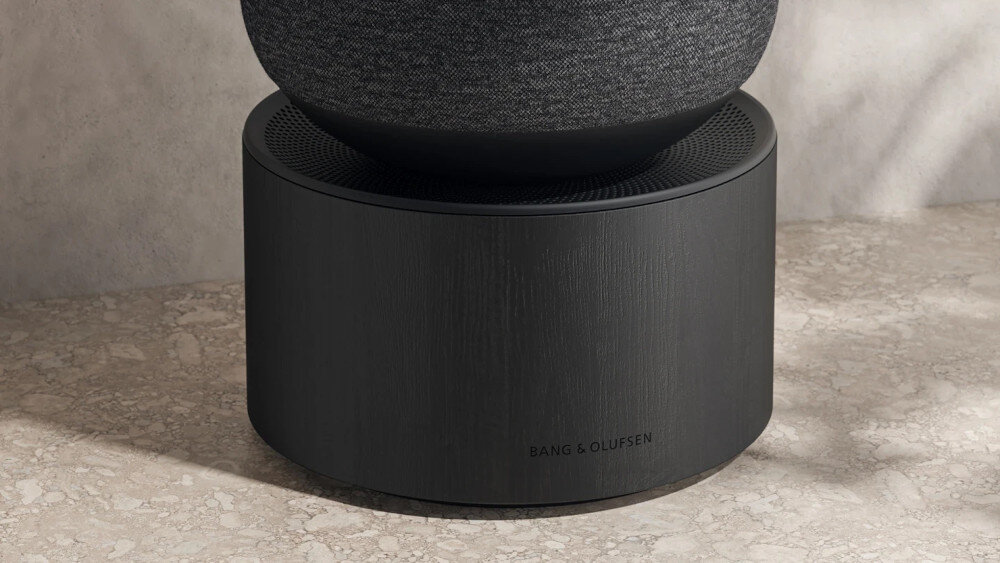 Czarny głośnik o cylindrycznym kształcie z widocznym logo \'BANG & OLUFSEN\' na dolnej części. Górna część pokryta jest materiałem tekstylnym.