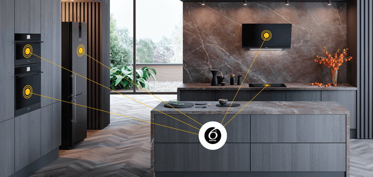 Nowoczesna kuchnia z ciemnymi szafkami i wyspą kuchenną, na której znajdują się naczynia. Na ścianie widać okap, a w tle duże okno z widokiem na zieleń.