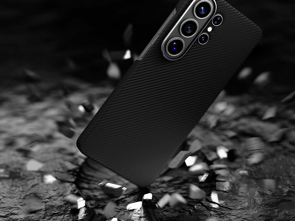 Smartfon Samsung Galaxy S w etui z włókna aramidowego upadający na ziemię, efekt kruszącego się podłoża sugerujący wysoką odporność na uderzenia