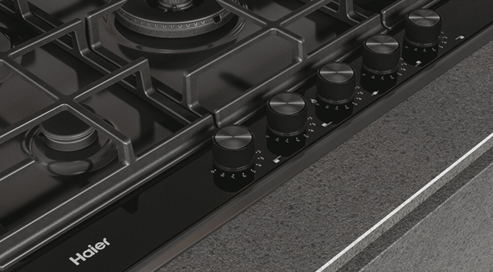 Na obrazie widoczna jest płyta gazowa z pięcioma pokrętłami do regulacji płomienia. Na powierzchni płyty znajduje się logo \'Haier\'.