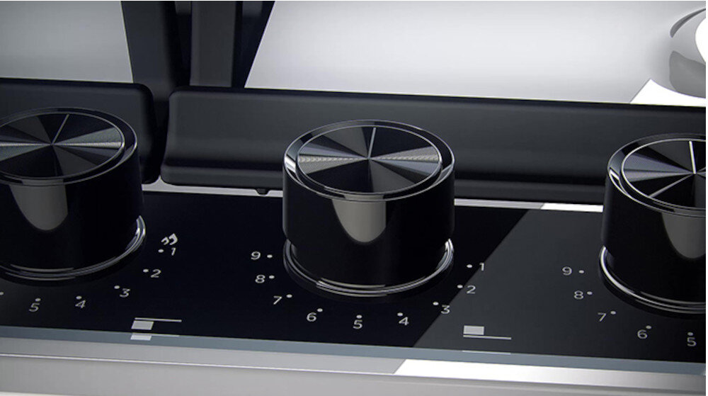 Obraz przedstawia zbliżenie na panel sterowania płyty gazowej z trzema czarnymi pokrętłami. Na panelu widoczne są oznaczenia liczbowo-graficzne od 1 do 9.