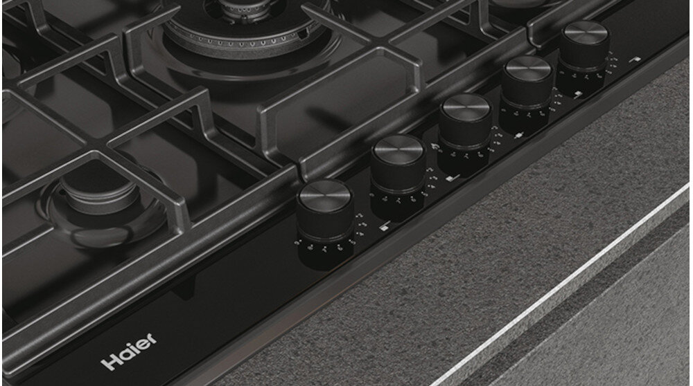 Czarna płyta gazowa z pięcioma pokrętłami i metalowymi rusztami. Widoczne logo: Haier.