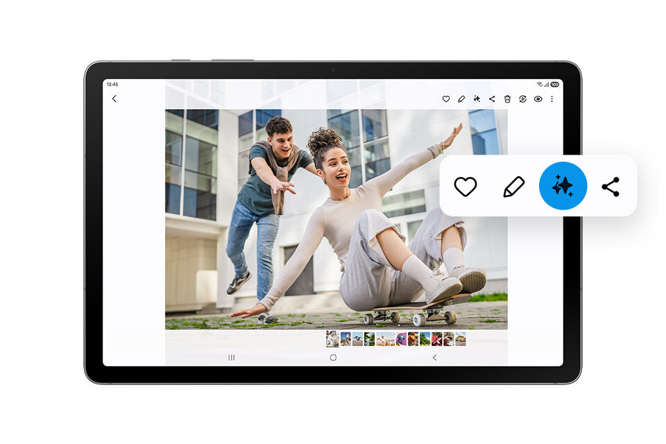 Tablet wyświetla zdjęcie dwóch osób, z których jedna siedzi na deskorolce, a druga ją popycha. Na ekranie widoczne są ikony edycji i udostępniania zdjęcia.