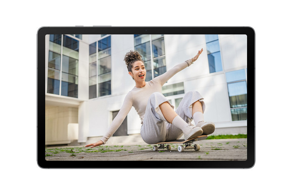 Tablet wyświetla obraz osoby jeżdżącej na deskorolce przed nowoczesnym budynkiem. Ekran urządzenia jest włączony, a ramka tabletu jest cienka.