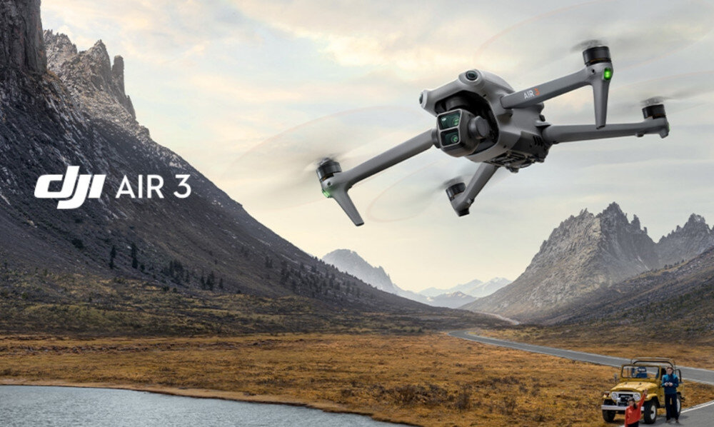 Na tle górskiego krajobrazu unosi się dron z widocznymi wirnikami. Obok drona znajduje się napis \'DJI AIR 3\'.