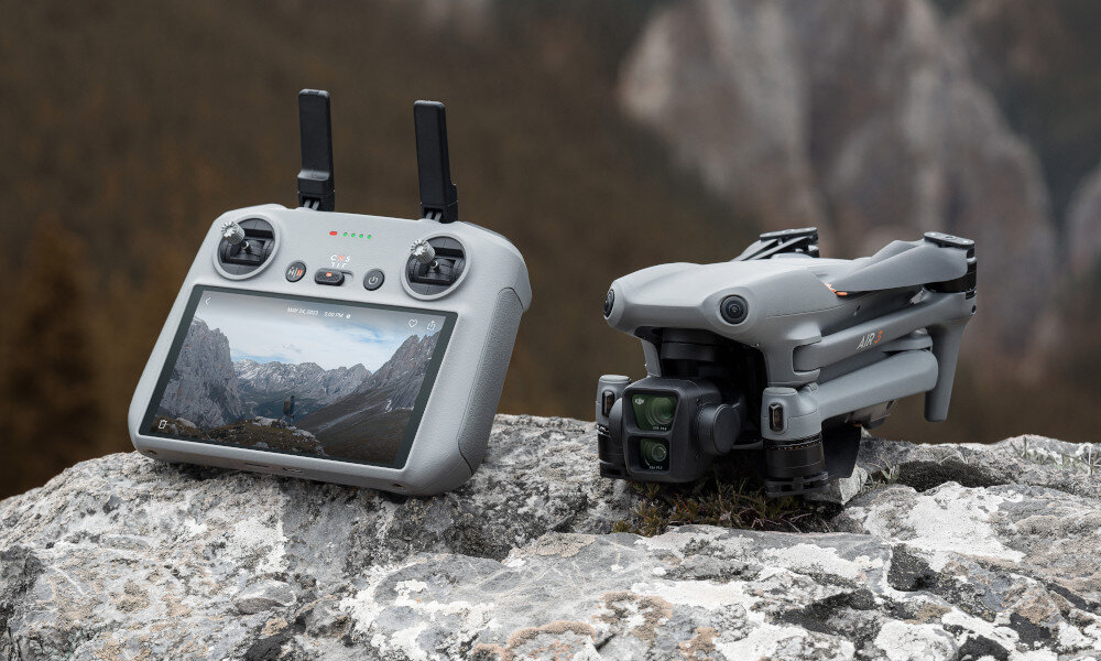 Na kamieniu leży złożony dron oraz kontroler z ekranem wyświetlającym krajobraz górski. Oba urządzenia są w kolorze szarym.