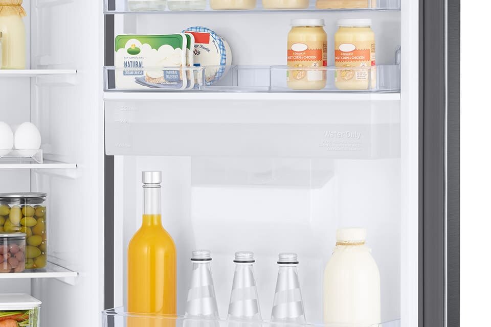 Wnętrze lodówki z widocznymi półkami, na których znajdują się różne produkty spożywcze, takie jak słoiki, butelki z napojami i jajka. Na drzwiach lodówki widoczny jest napis \'Water Only\'.