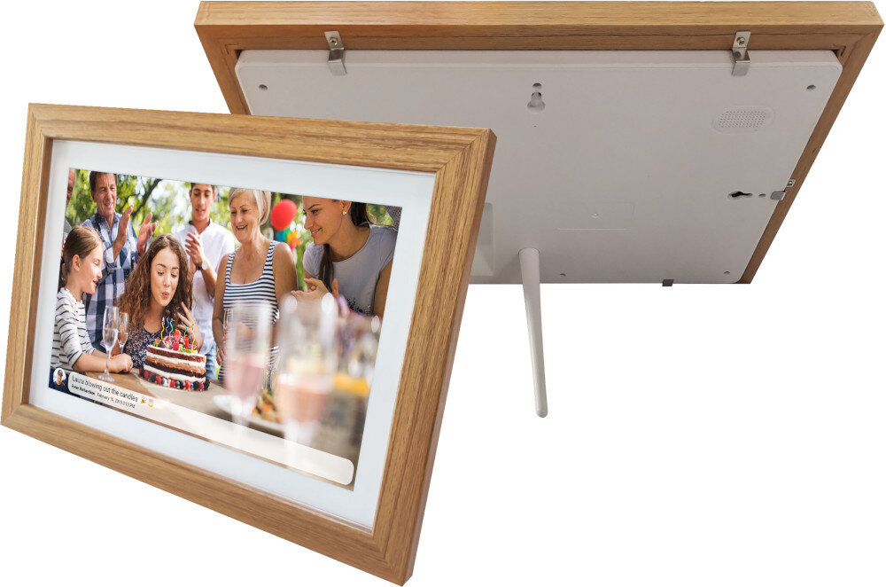 Na obrazie widoczna jest cyfrowa ramka w kolorze brązowym z wyświetlanym zdjęciem przedstawiającym grupę osób przy torcie. Ramka ma drewnianą obudowę i białe tło wokół ekranu.