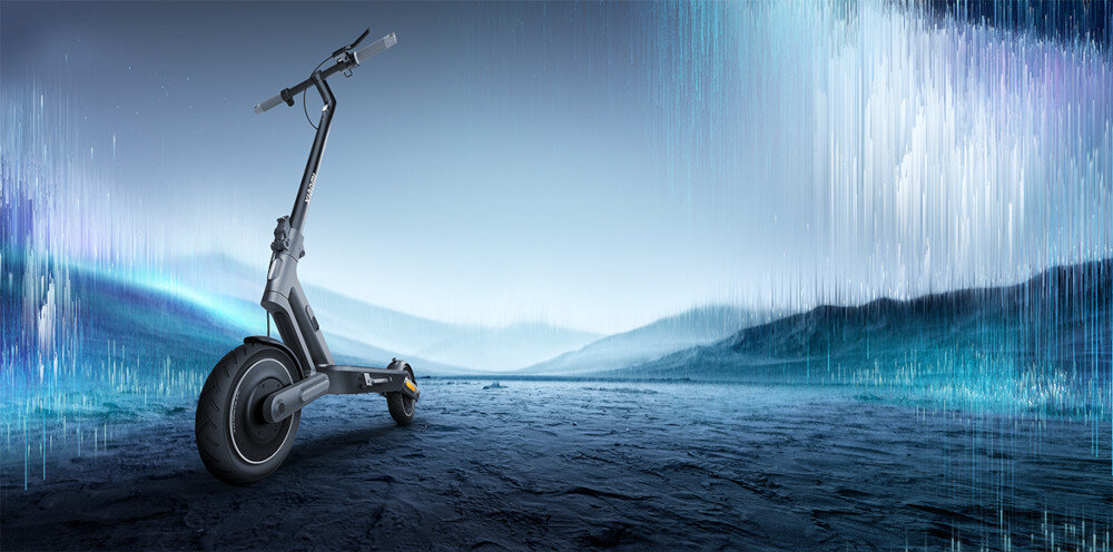 Czarna hulajnoga elektryczna stoi na tle futurystycznego krajobrazu z niebieskimi i białymi świetlnymi efektami. Tło przedstawia rozmyte wzgórza i niebo z pionowymi liniami świetlnymi.