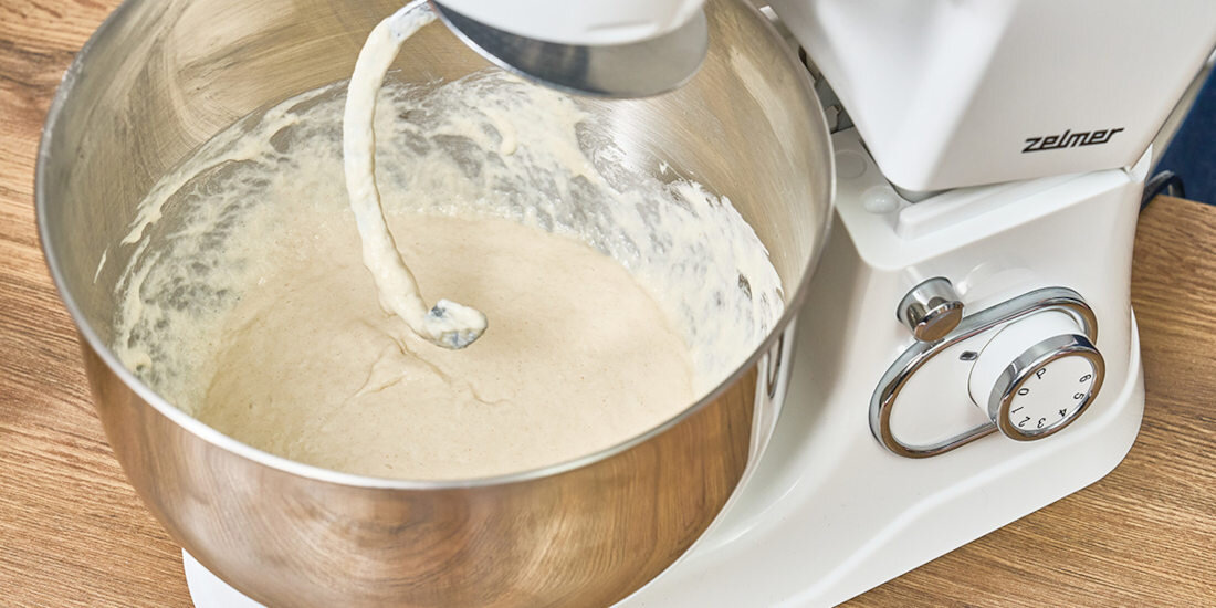 Na obrazie widoczny jest robot kuchenny z misą wypełnioną ciastem, a na urządzeniu znajduje się logo \'zelmer\'.