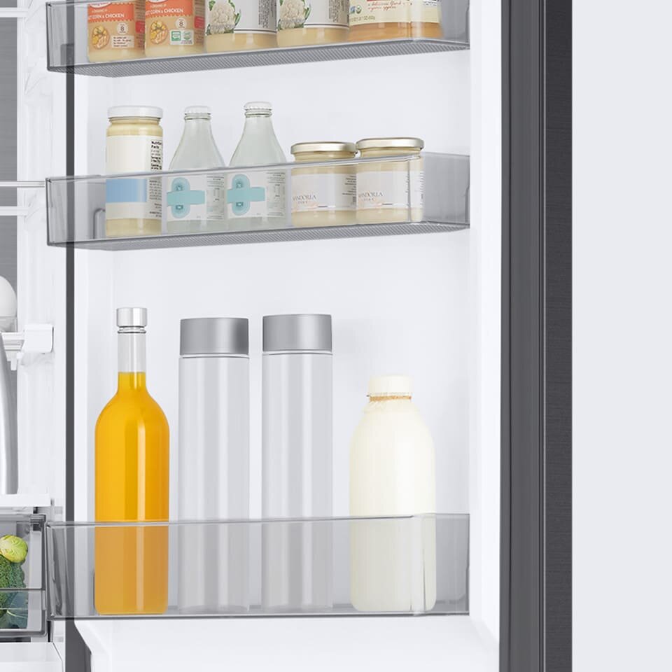 Wnętrze lodówki z trzema półkami na drzwiach, na których znajdują się różne produkty spożywcze, w tym butelki i słoiki. Produkty są uporządkowane, a wnętrze lodówki jest jasne i przestronne.