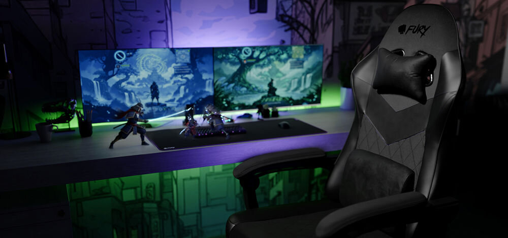 Czarny fotel gamingowy z logo \'FURY\' stoi przed biurkiem z dwoma monitorami wyświetlającymi grafikę z grą. Biurko jest oświetlone zielonym światłem, a na nim znajdują się figurki i klawiatura.