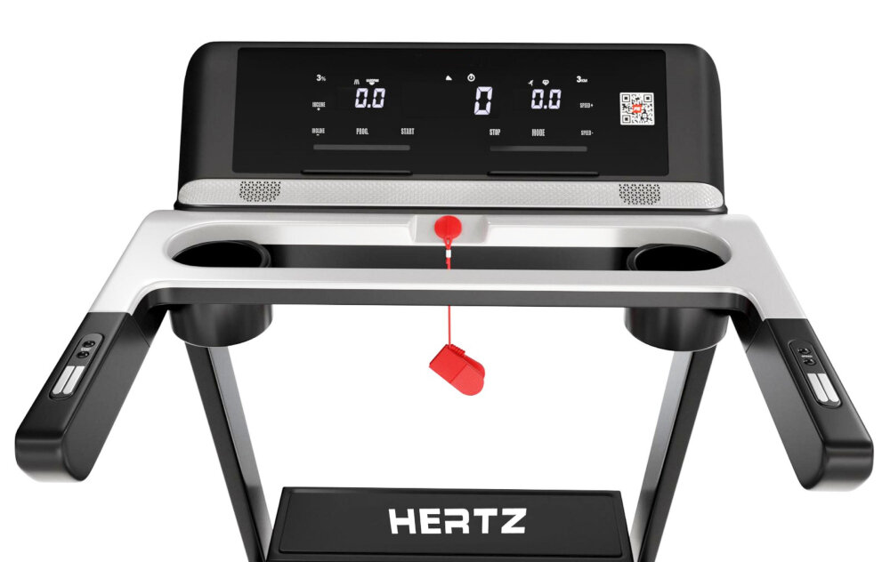 Panel sterowania bieżni z wyświetlaczem pokazującym wartości 0.0 oraz przyciski funkcyjne. Na dolnej części widoczne jest logo \'HERTZ\'.