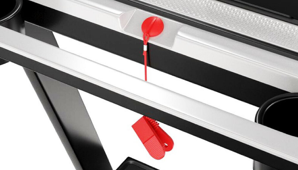 Część bieżni elektrycznej z widocznym czerwonym klipsem bezpieczeństwa przymocowanym do panelu sterowania. Obok znajduje się uchwyt na napoje.