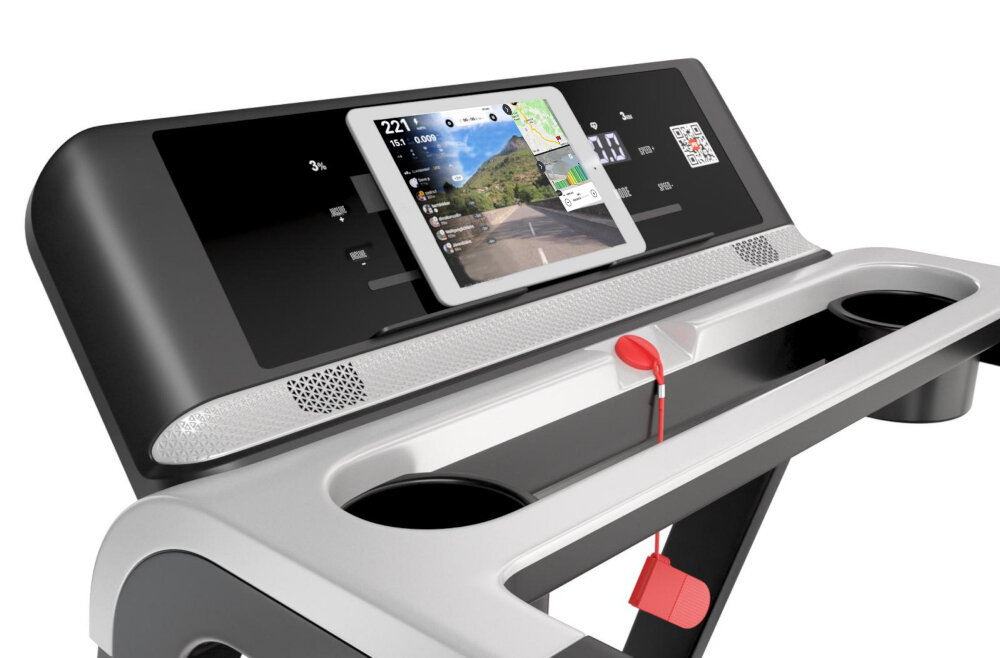 Panel sterowania bieżni z wbudowanym uchwytem na tablet, na którym wyświetlana jest aplikacja z trasą biegową. Obok znajdują się dwa uchwyty na napoje oraz czerwony klucz bezpieczeństwa.