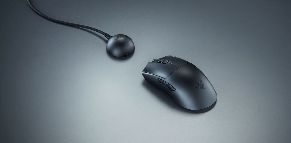 Na obrazie widoczna jest czarna mysz komputerowa z logo producenta oraz okrągła stacja dokująca z podłączonym kablem. Powierzchnia jest gładka, a mysz ma kilka przycisków bocznych.