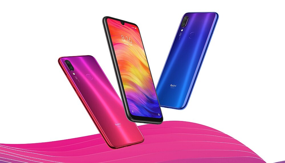 Trzy smartfony w różnych kolorach (czerwony, niebieski, fioletowy) unoszą się na tle gradientu w odcieniach różu. Na ekranie jednego z telefonów widoczna jest godzina 8:16.