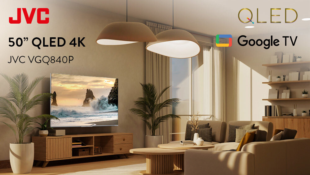 W salonie znajduje się telewizor wyświetlający krajobraz z morzem i skałami, umieszczony na drewnianej szafce. Na obrazie widoczne są napisy: \'JVC\', \'50” QLED 4K\', \'JVC VGQ840P\', \'QLED\', \'Google TV\'.