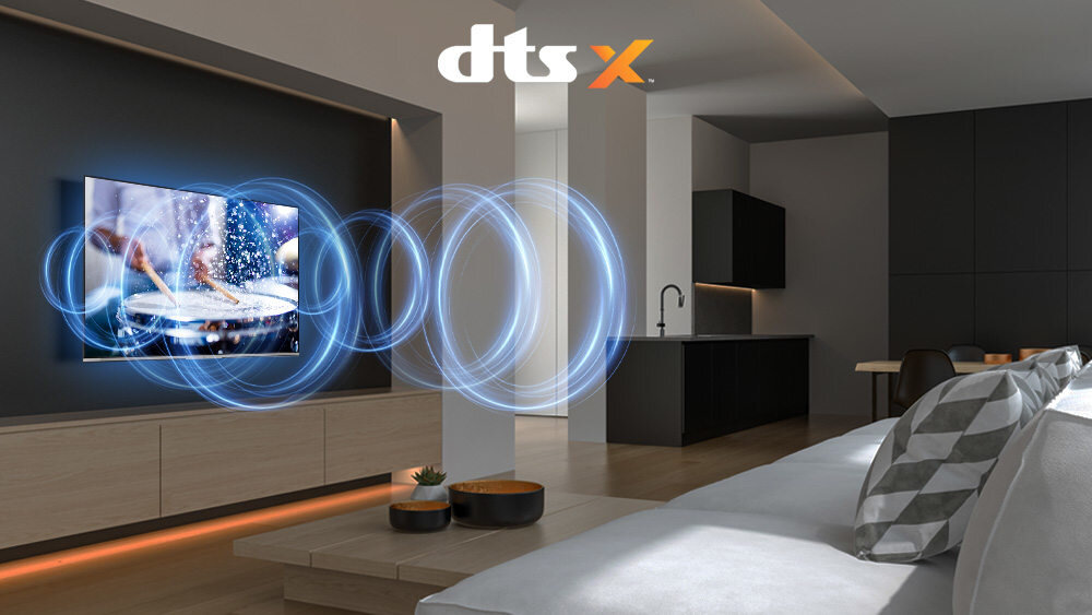 W nowoczesnym salonie znajduje się telewizor wyświetlający obraz z efektami dźwiękowymi przedstawionymi jako niebieskie fale. Na górze obrazu widnieje logo \'dts X\'.
