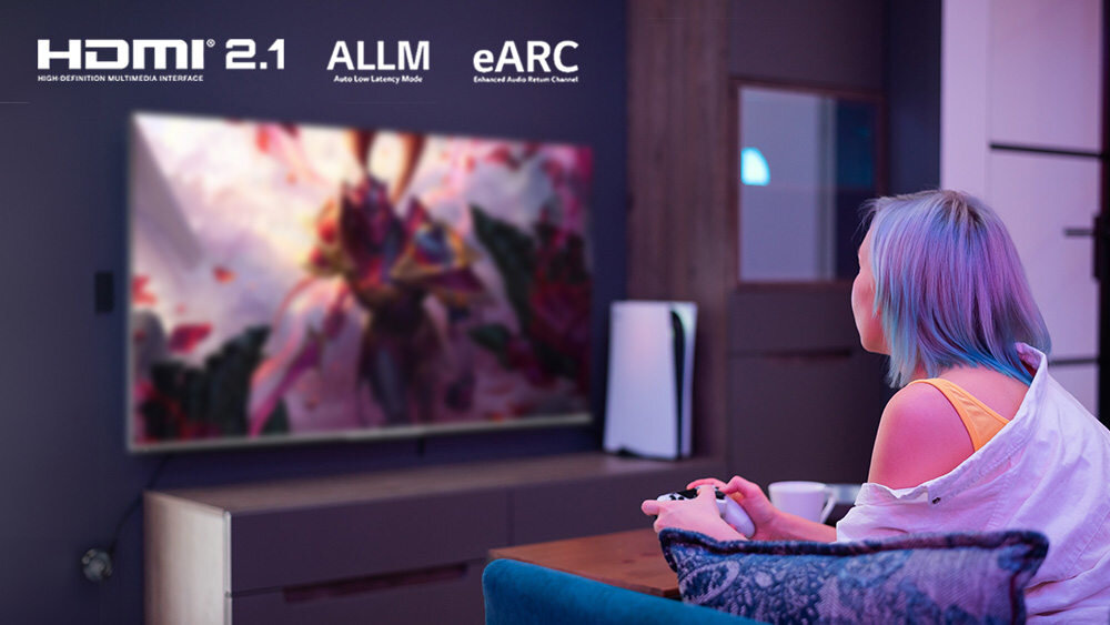 Osoba siedzi na kanapie i gra na konsoli, patrząc na duży telewizor z dynamicznym obrazem. Na ekranie widoczne są napisy: \'HDMI 2.1\', \'ALLM\', \'eARC\'.