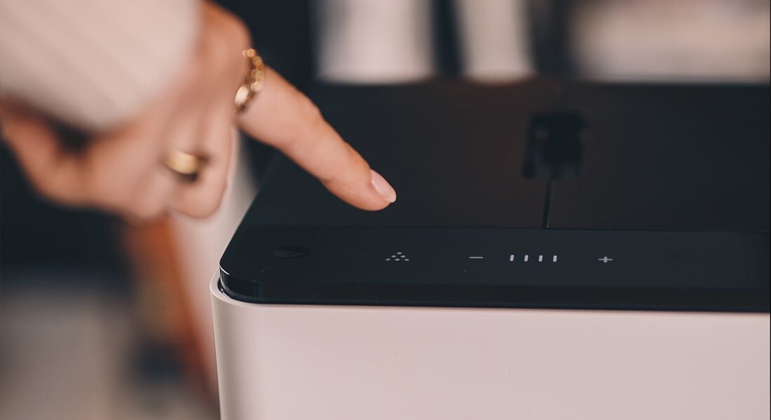 Zbliżenie na panel dotykowy ekspresu do kawy z widocznymi symbolami i przyciskami. Palec wskazuje na jeden z przycisków na panelu.