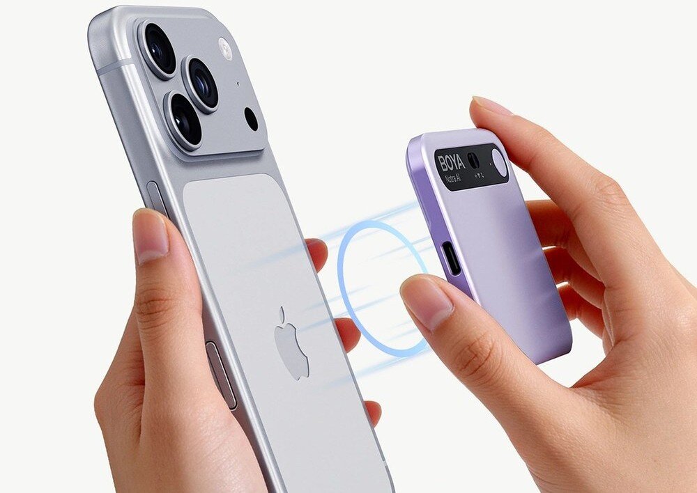 Dyktafon AI BOYA Notra Zbliżenie na dłonie trzymające srebrny smartfon marki Apple oraz zbliżające do jego pleców małe, fioletowe, prostokątne akcesorium, między którymi widoczne są jasnoniebieskie linie symbolizujące przyciąganie magnetyczne, sztuczna inteligencja, pakiety, integracja z AI