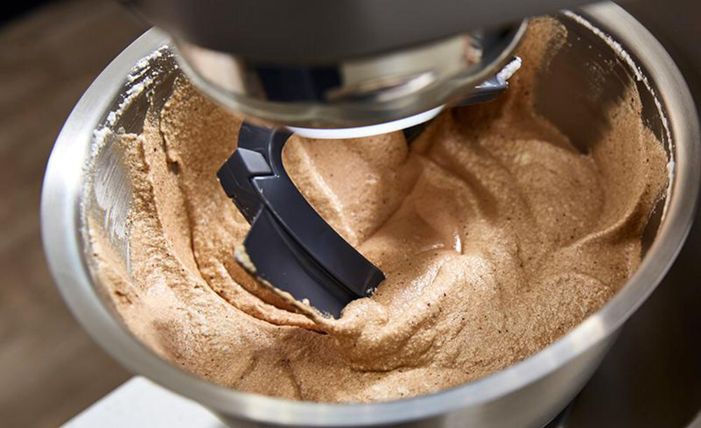 Misa robota kuchennego z mieszadłem, wypełniona jasnobrązową masą. Mieszadło jest w trakcie mieszania składników.