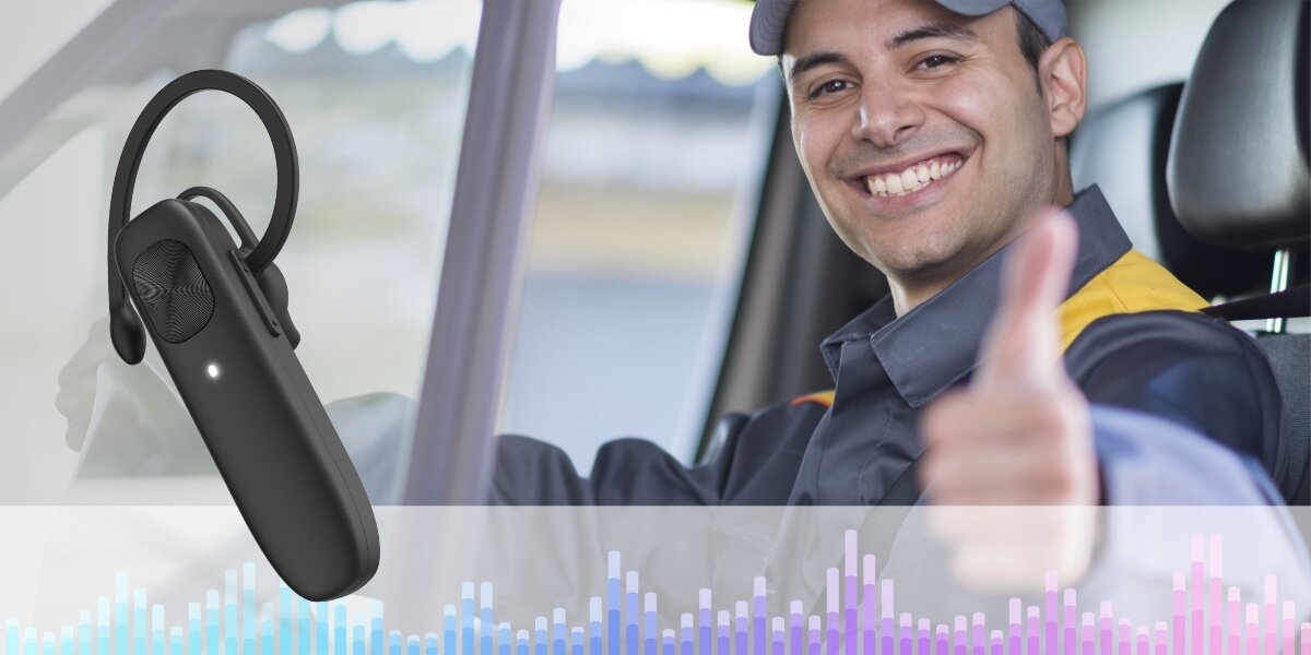 Na pierwszym planie widoczna jest czarna słuchawka z mikrofonem i zaczepem na ucho. W tle znajduje się osoba w czapce, uśmiechająca się i pokazująca kciuk w górę.