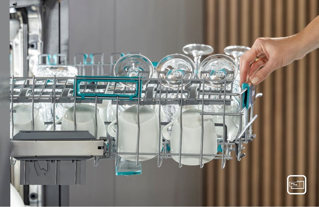 Osoba wyciąga górny kosz zmywarki, w którym znajdują się szklanki i kubki. W prawym dolnym rogu widoczna jest ikona z symbolem zmywarki.