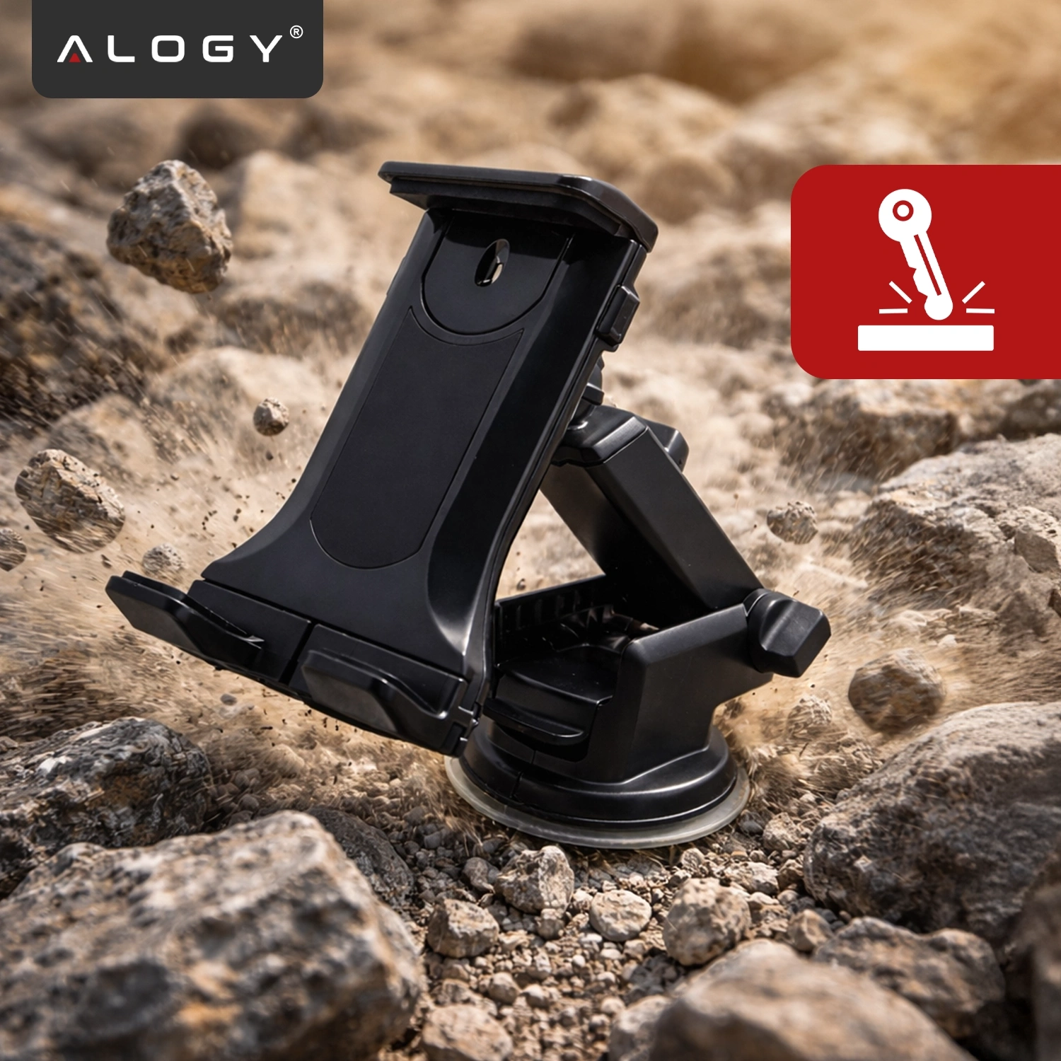 Czarny uchwyt samochodowy na telefon i tablet z logo \'ALOGY\' jest umieszczony na kamienistym podłożu. Obok znajduje się czerwony symbol przedstawiający dźwignię na białym tle.