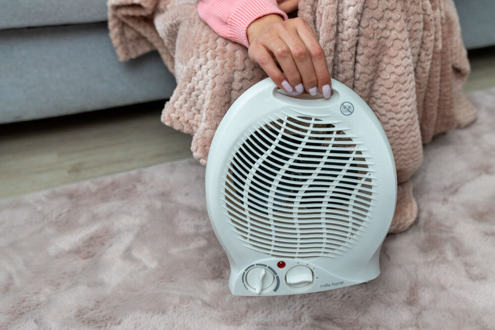 Osoba trzyma biały termowentylator z widocznymi pokrętłami i napisem \'milla home\'.