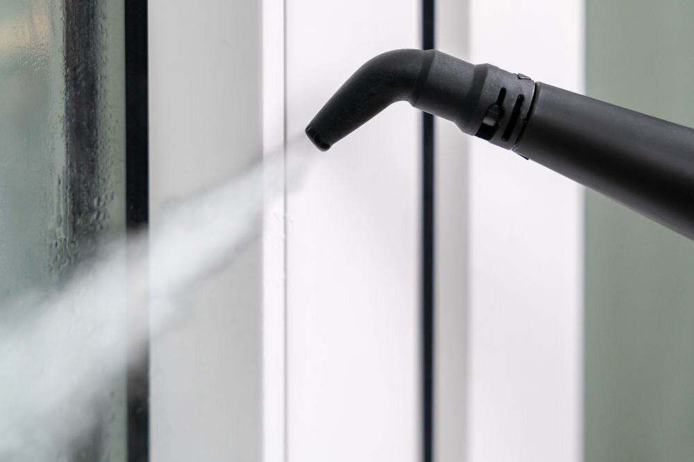 ODKURZACZ PIORĄCY SPOTCLEAN GOTZE&JENSEN CSC600 z ekranem LED komunikatami głosowymi powiadomieniem o pełnym zbiorniku intuicyjną obsługą Zbliżenie na czarną dyszę kątową emitującą parę w celu wyczyszczenia zakamarka ramy białego okna.