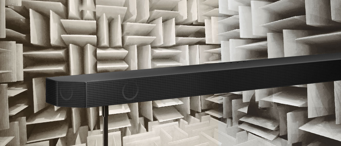 Czarny soundbar umieszczony na tle pomieszczenia z panelami akustycznymi w kształcie prostokątnych bloków.