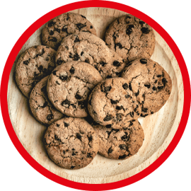 Na drewnianym talerzu znajduje się stos ciastek z kawałkami czekolady. Obraz jest otoczony czerwoną ramką.