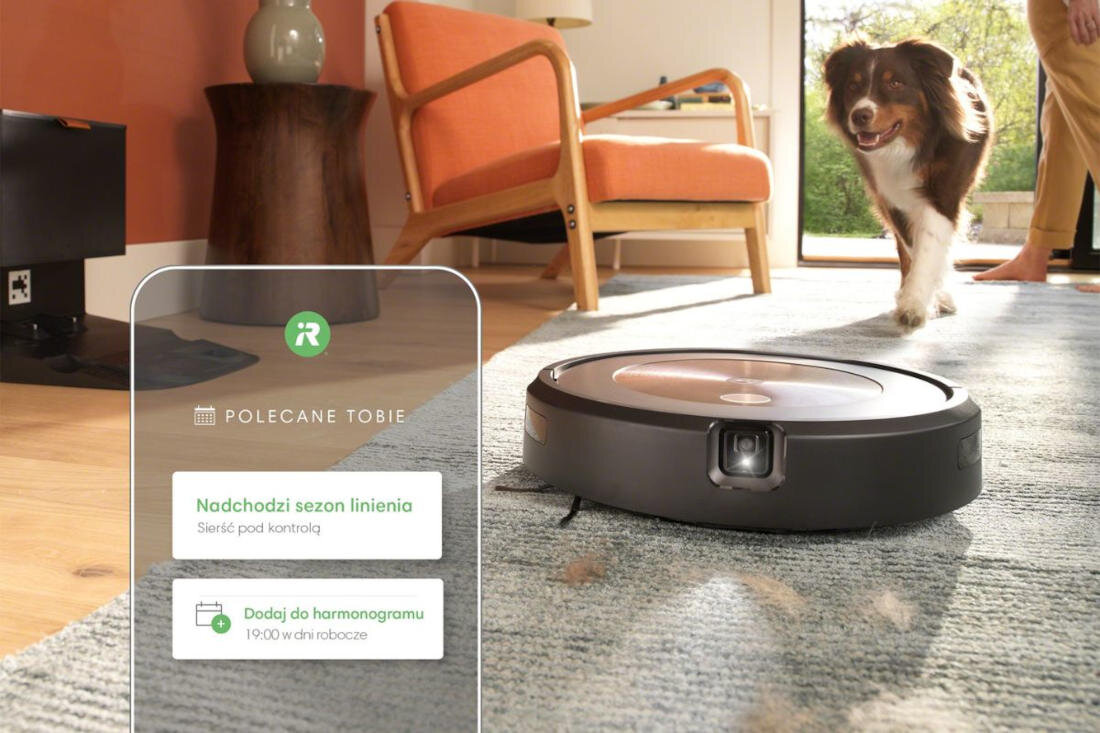 Na dywanie w salonie znajduje się robot sprzątający. Obok widoczny jest tekst: \'Polecane Tobie\', \'Nadchodzi sezon linienia\', \'Sierść pod kontrolą\', \'Dodaj do harmonogramu\', \'19:00 w dni robocze\'.