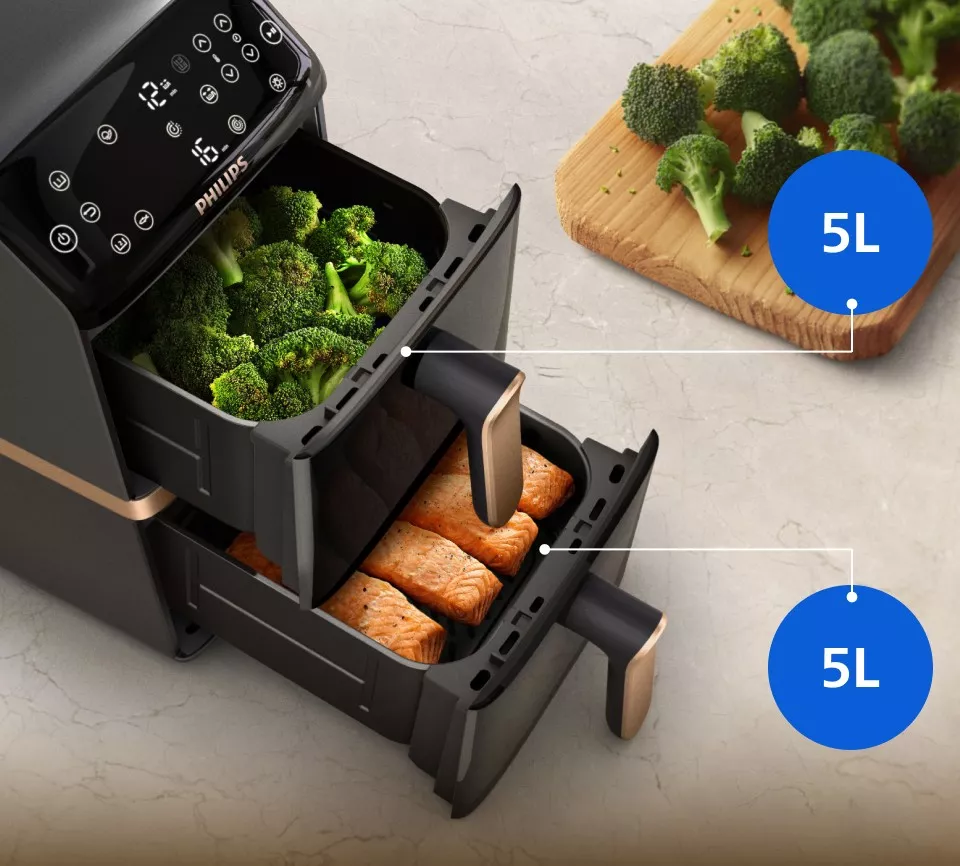 Na obrazie widoczna jest frytkownica beztłuszczowa z dwoma wysuniętymi koszami, w jednym z nich znajdują się brokuły, a w drugim kawałki łososia. Na urządzeniu widnieje logo \'PHILIPS\', a obok koszyków znajdują się oznaczenia \'5L\'.