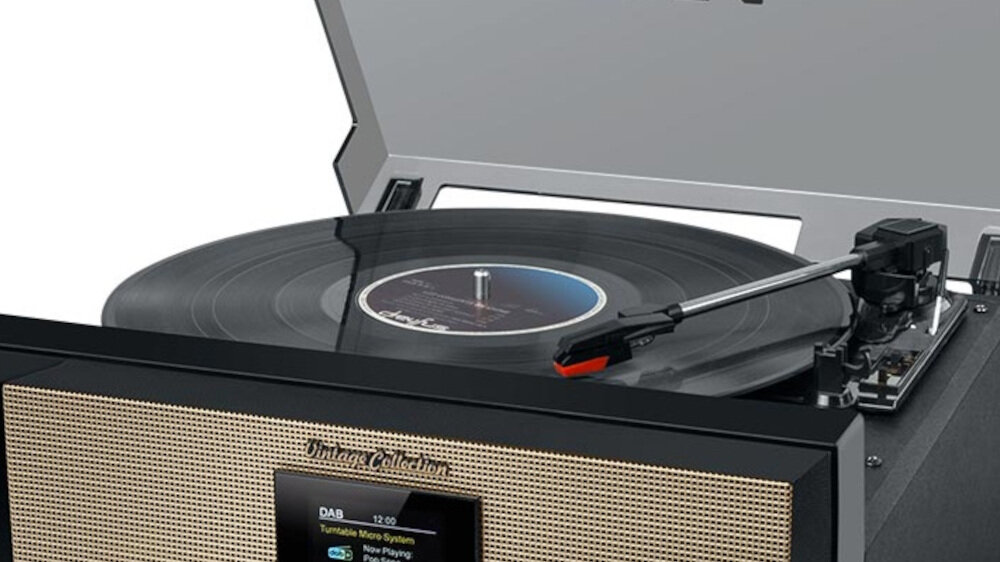 Gramofon z czarną płytą winylową na talerzu, z widocznym ramieniem i igłą. Na froncie urządzenia znajduje się napis \'Vintage Collection\' oraz wyświetlacz z tekstem \'DAB 12:00 Turntable Micro System Now Playing\'.