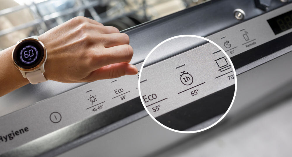 Osoba dotyka panelu sterowania zmywarki, na którym widoczne są symbole programów: Eco 55°, 1h 65°, oraz ikony związane z temperaturą i czasem. Na ręce znajduje się zegarek z wyświetlaczem pokazującym liczbę 60.
