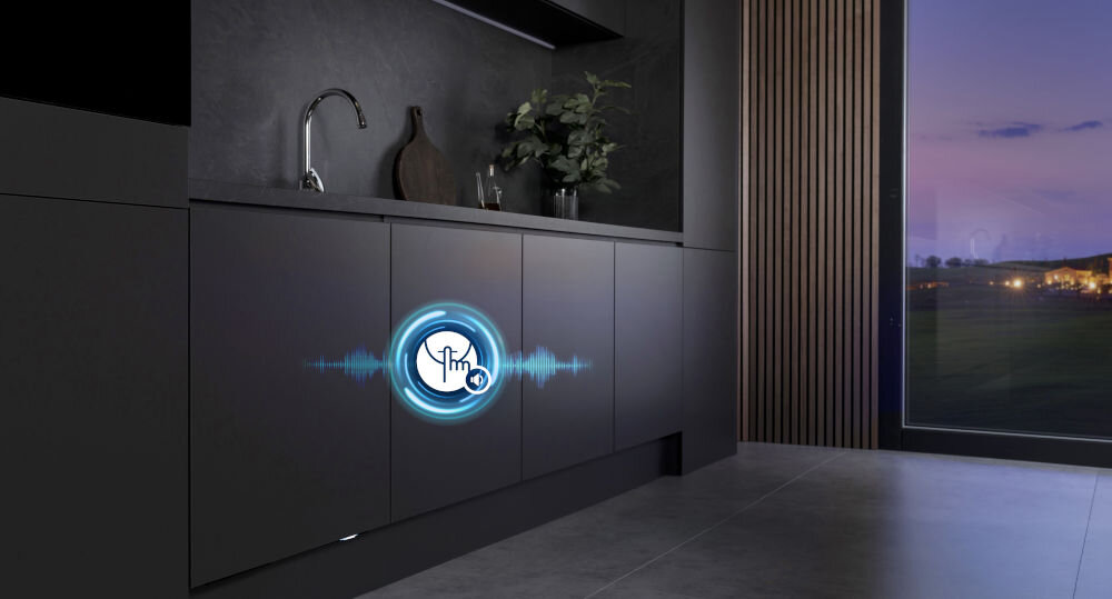 Kuchnia z ciemnymi szafkami, na jednej z nich widoczna jest grafika z symbolem dłoni i falą dźwiękową. W tle znajduje się duże okno z widokiem na zewnątrz.