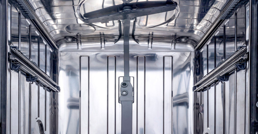 Wnętrze zmywarki z widocznym metalowym ramieniem spryskującym i błyszczącymi, stalowymi ścianami. Widać również prowadnice na bocznych ścianach.