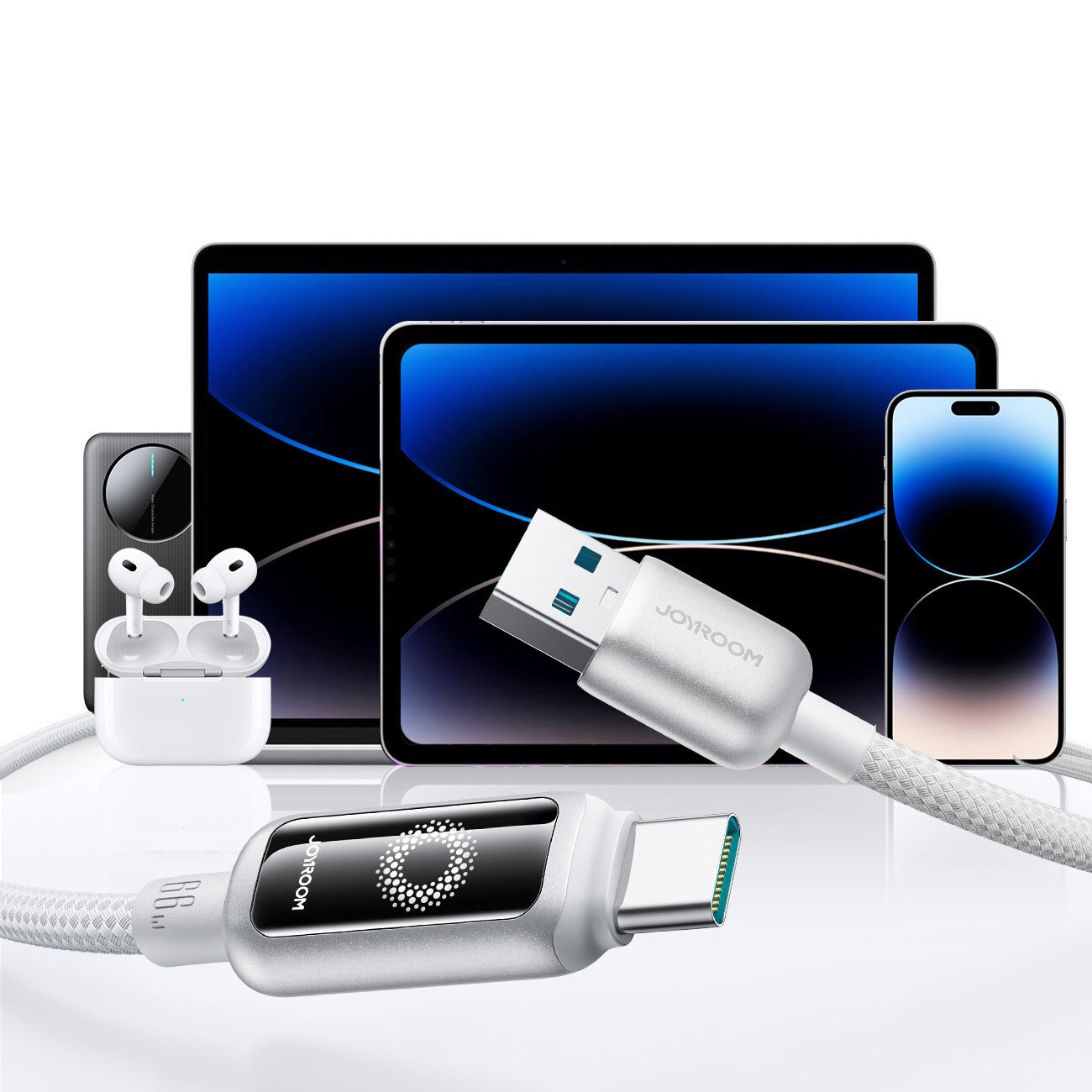 Na obrazie widoczny jest kabel USB-A do USB-C z napisem \'JOYROOM\', otoczony różnymi urządzeniami elektronicznymi, takimi jak smartfon, tablet i słuchawki bezprzewodowe. Kabel ma srebrny oplot i wyświetlacz LED z wzorem okręgu.