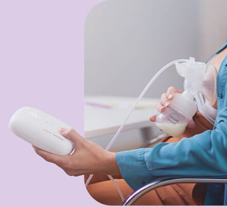 Osoba trzyma laktator z butelką wypełnioną mlekiem, połączony przewodem z urządzeniem w dłoni. Na butelce widoczny jest napis \'Philips Avent\'.