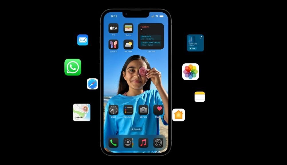 Smartfon z wyświetlaczem prezentującym ekran główny z ikonami aplikacji i zdjęciem osoby trzymającej różowy makaronik. Wokół telefonu unoszą się ikony aplikacji, takie jak WhatsApp, Mail i Zdjęcia.