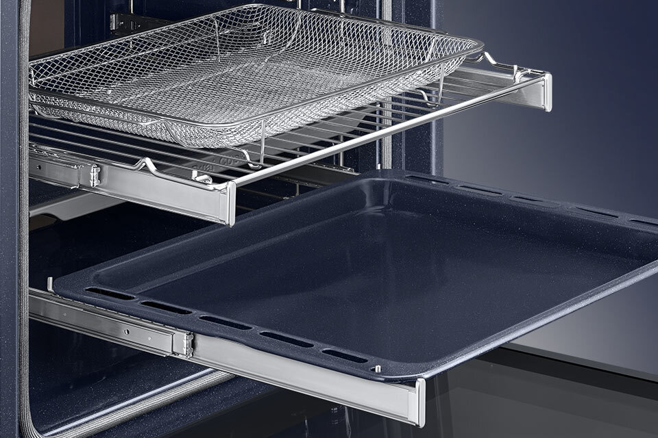 Wnętrze piekarnika z wysuniętymi dwoma półkami: górna z metalowym koszem, dolna z ciemną blachą do pieczenia.