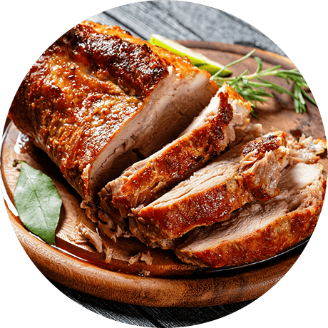 Na drewnianej desce leży pieczone mięso pokrojone w plastry, obok znajduje się gałązka rozmarynu i liść laurowy.