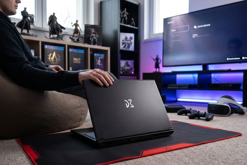 Osoba korzysta z laptopa DREAMMACHINES RT5050 podczas rozgrywki gamingowej w pokoju z konsolą - dźwięk Sound Blaster Studio+