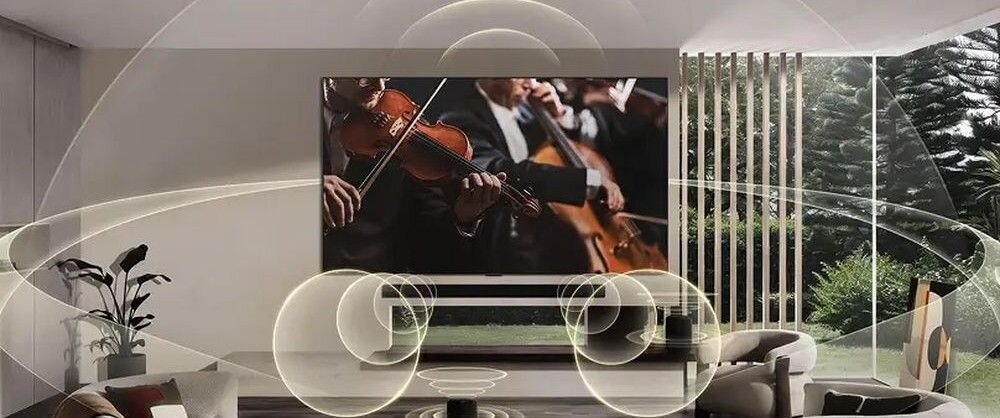 W salonie na ścianie wisi duży telewizor, na którym wyświetlany jest obraz orkiestry grającej na instrumentach smyczkowych. Wokół telewizora i w pomieszczeniu widoczne są graficzne fale dźwiękowe, a za oknem widać drzewa.